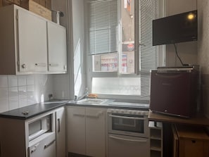 A kitchen with white cabinets, a microwave, an oven, a sink, and a television mounted on the wall. - Central studio for 4 guests - Cauterets centre (Cauterets)