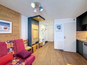 A compact living space with a sofa, a small dining table, a kitchenette, and a door leading to another room. - Les Menuires - Cozy studio for 4 guests (Les Menuires)