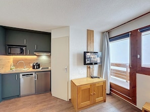 A compact kitchen with modern appliances, a wooden cabinet, and a television mounted on the wall. - Les Menuires - Cozy studio for 4 guests (Les Menuires)