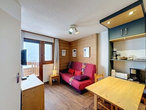 A compact room with a wooden floor, a sofa, a small table, a TV, and a kitchenette with a stove and coffee maker. - Les Menuires - Cozy studio for 4 guests (Les Menuires)