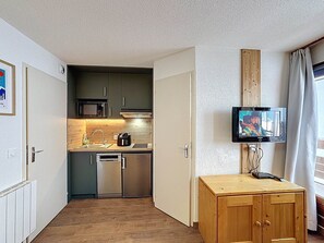 A compact kitchen with a microwave, stove, and dishwasher. A television is mounted on the wall, and a wooden cabinet is visible. - Les Menuires - Cozy studio for 4 guests (Les Menuires)