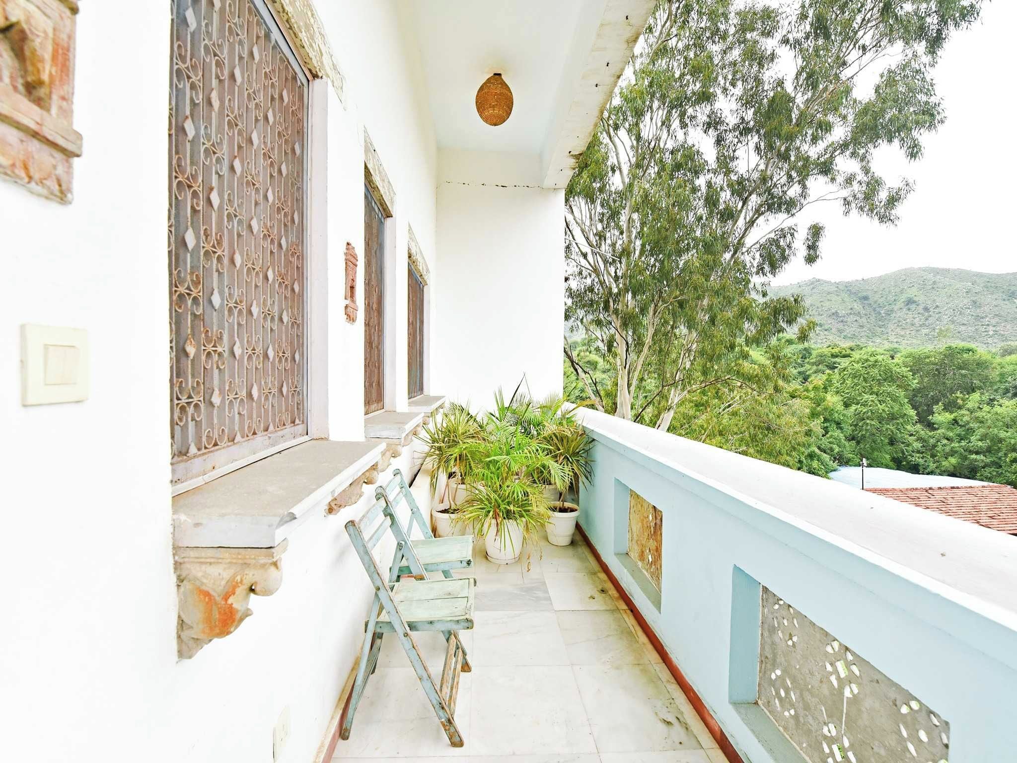 A balcony with potted plants, a wooden chair, and a view of a green landscape.
