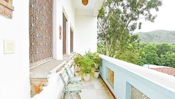 A balcony with potted plants, a wooden chair, and a view of a green landscape.