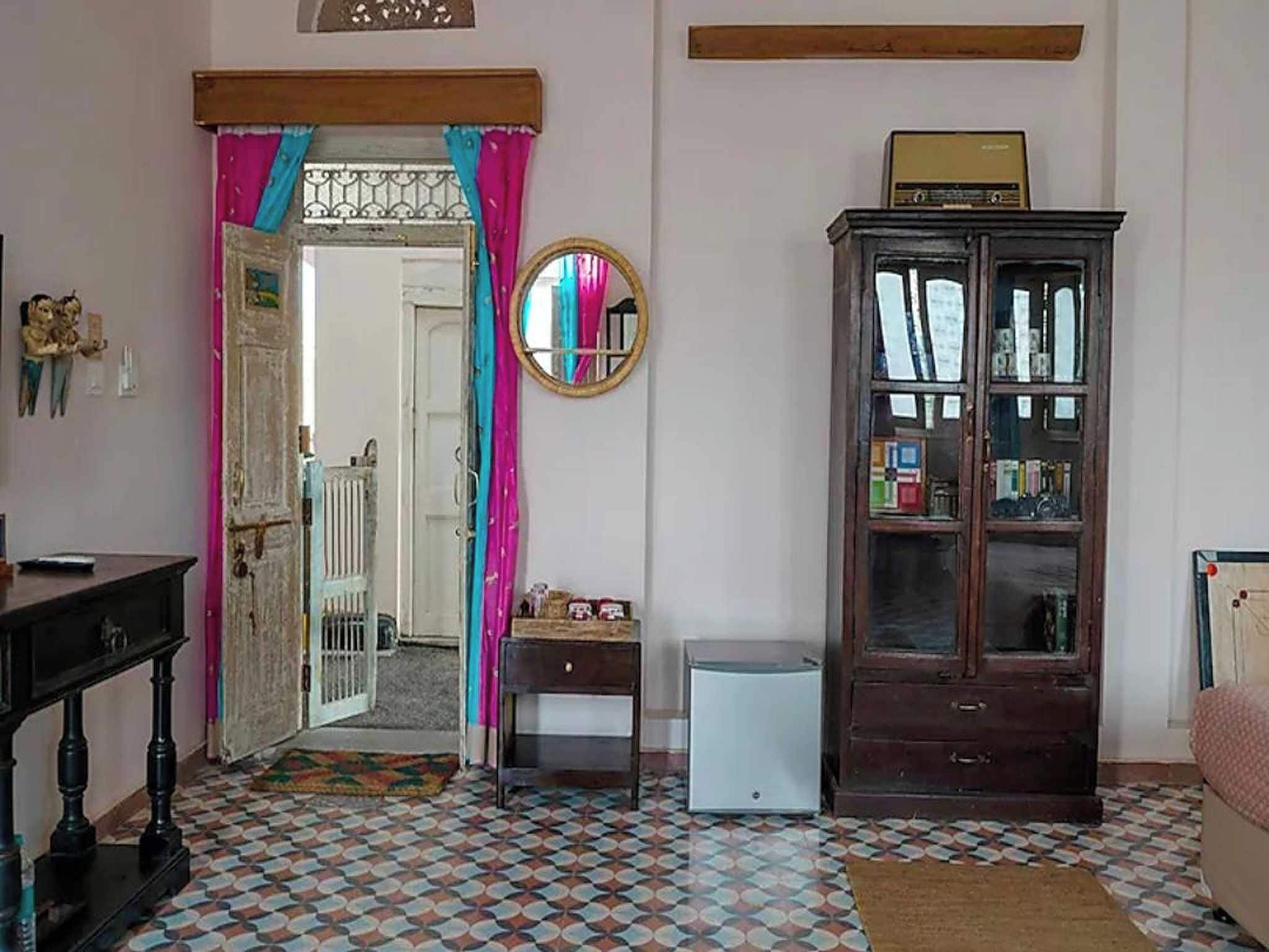 Una habitación con piso estampado, un mueble de madera, un electrodoméstico blanco pequeño y una puerta que da a otra habitación.