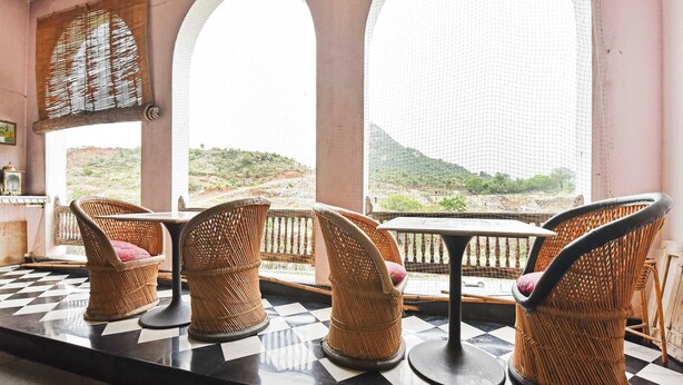 Un espacio de estar con sillas de mimbre y piso a cuadros, con vistas a un paisaje montañoso a través de amplios ventanales.