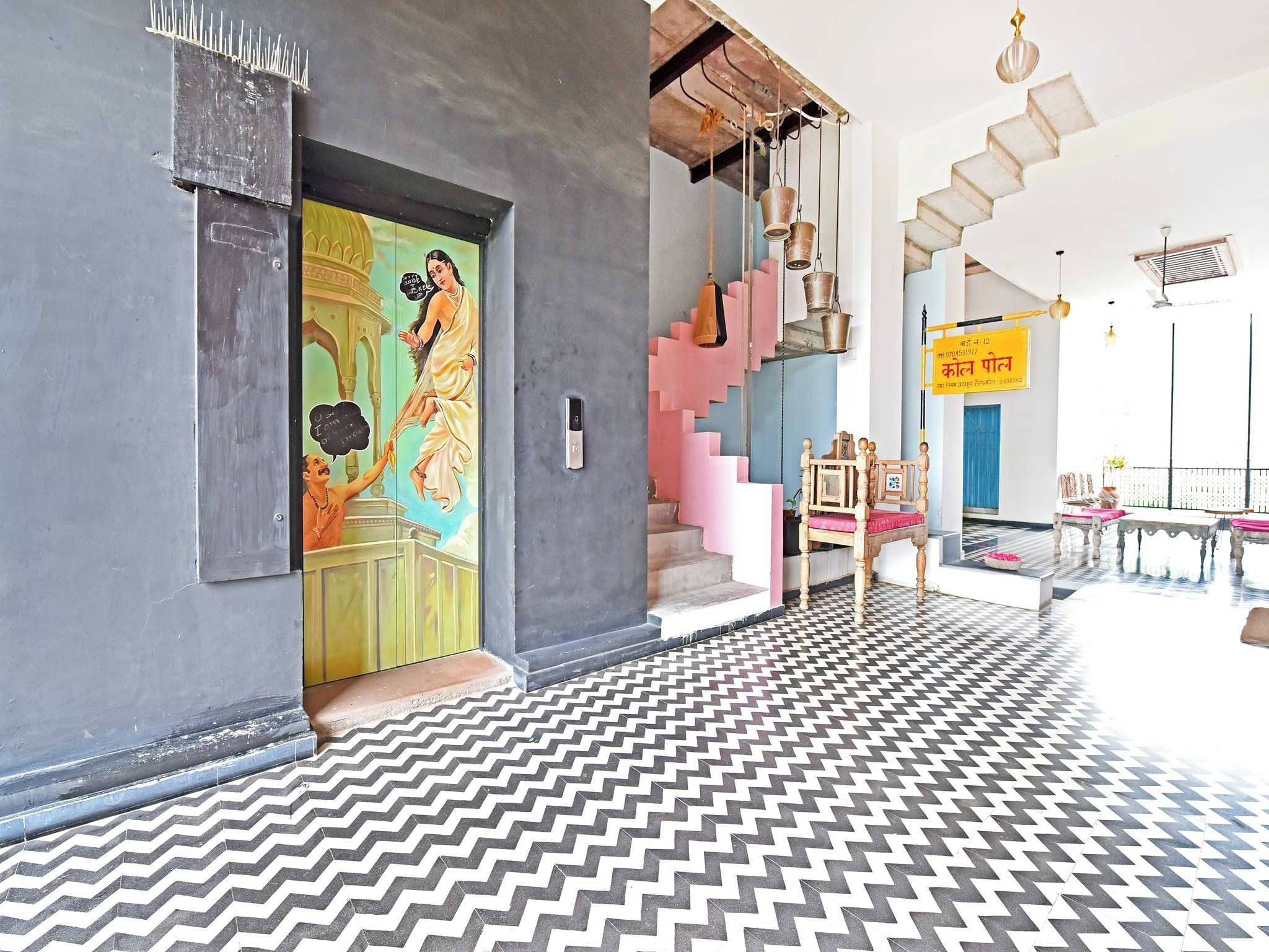A modern interior with a chevron-patterned floor, a staircase with pink steps, and a traditional Indian painting on the wall.