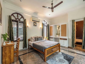 A bedroom with a bed, a desk, a chair, a ceiling fan, and a window with curtains.