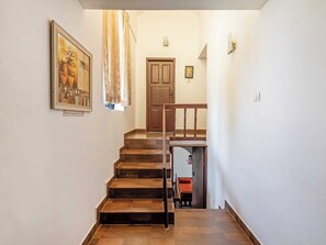 A staircase with wooden steps leading to a door, a framed picture on the wall, and a small table with a cushion.