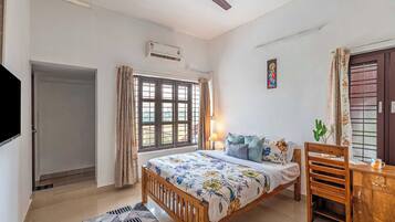 Un dormitorio con cama, escritorio, silla, ventilador de techo, ventana con cortinas, equipo de aire acondicionado y puerta.