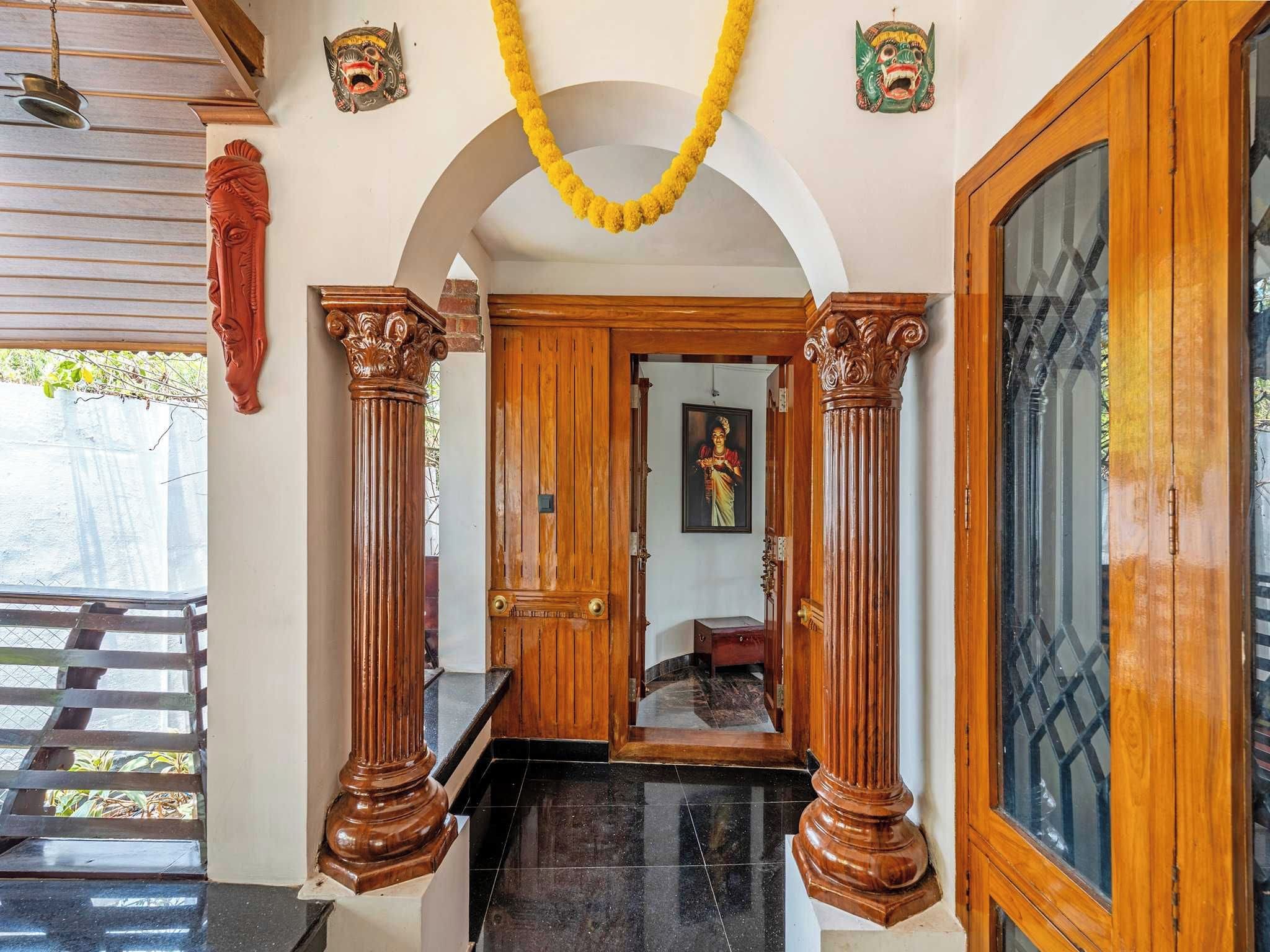 Una entrada tradicional con columnas de madera, un vano y un espejo que refleja a una persona.