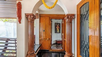 Una entrada tradicional con columnas de madera, un vano y un espejo que refleja a una persona.