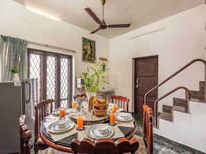 A dining area with a round table set for four, surrounded by chairs, a ceiling fan, and a door with a metal gate.