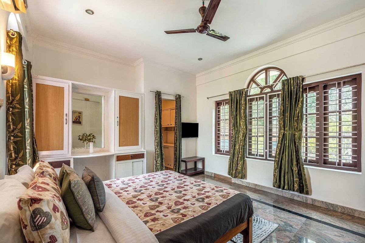 Un dormitorio con cama, armario, televisor y ventana con cortinas.
