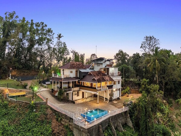 A multi-story house with a swimming pool, surrounded by lush greenery.