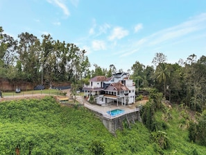 Una casa moderna de varios pisos con piscina, rodeada de exuberante vegetación y árboles.