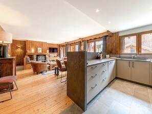 A modern kitchen with wooden cabinetry, a dining area with a table and chairs, and a living room with a sofa and fireplace. - Charming apartment - 7 guests, south terrace (Val-d'Isère)