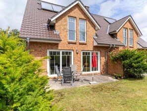 Ein zweistöckiges Haus mit Ziegelaußenwand, einem Ziegeldach und einer überdachten Terrasse mit Gartenmöbeln.