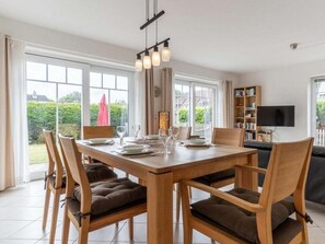 Ein Essbereich mit einem Holztisch und Stühlen, einer Chandelier und Blick ins Freie durch große Fenster.