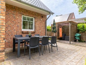 A brick house with a patio area featuring a table and chairs, a window, and a shed in the background. - Holiday Home With 3 Bedrooms (St. Peter-Ording)