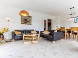 Ein modernes Wohnzimmer mit einer Sofagarnitur, einem Esstisch mit Stühlen, einer Stehlampe und einem Bild an der Wand.
