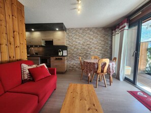 A modern living space with a red sofa, wooden coffee table, stone wall, and a kitchen area with wooden cabinets and a stone backsplash. - Ideal T2 apartment for 4 guests - Samoëns (Samoëns)