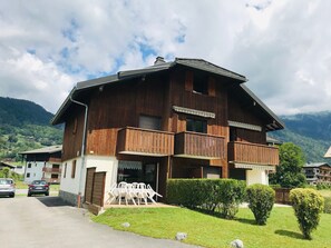 A two-story wooden building with balconies, a paved driveway, and a grassy area with chairs. - Ideal T2 apartment for 4 guests - Samoëns (Samoëns)