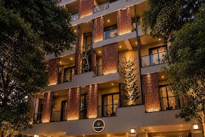 A multi-story hotel with balconies, a sign with a circular logo, and surrounding trees. - Elegant 1BR Apartment, Gurugram (Gurugram)