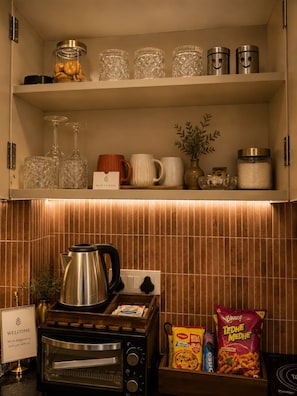 A kitchenette with a gas stove, a coffee maker, and a sign welcoming guests.
