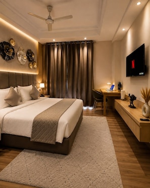 A modern hotel room with a large bed, a desk, a television, and a ceiling fan. - Elegant 1BR Apartment, Gurugram (Gurugram)