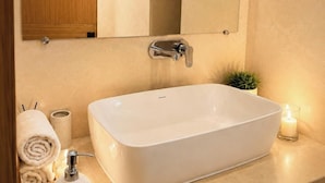 Ein Badezimmer mit einer weißen Badewanne, einem großen Spiegel, einem Holzschrank, einem kleinen Topfpflanzen und einer brennenden Kerze.