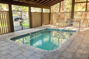 Ein Hallenbad mit Fliesenboden, einer Metallleiter und einem überdachten Bereich mit Stühlen.