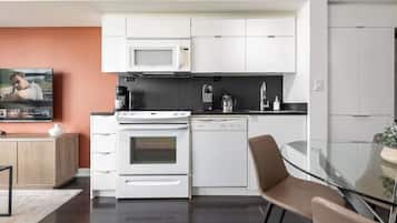 Cozinha moderna com eletrodomésticos brancos, mesa de jantar de vidro e televisão na parede.