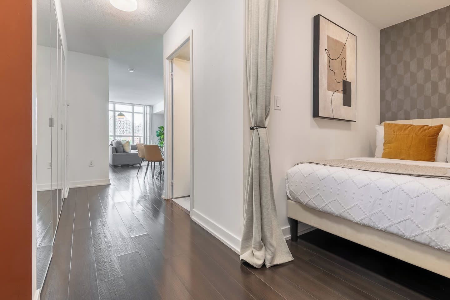 A hotel room with a bed, a painting on the wall, and a view of the city through large windows.