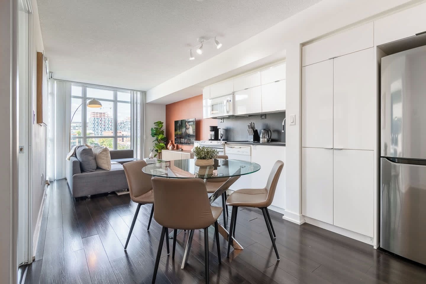 A modern kitchen with white cabinets, a stainless steel refrigerator, and a dining area with a glass table and chairs.