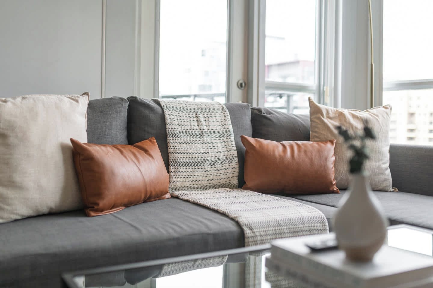 A modern living room with a grey sofa, multiple cushions, and a vase on a side table.