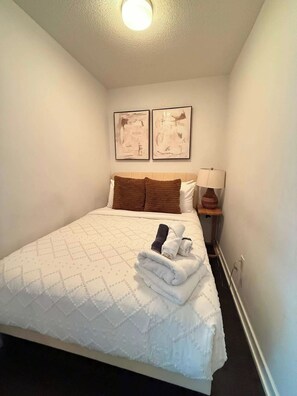 A hotel room with a bed, two wall-mounted artworks, a bedside lamp, and a folded towel on the bed.