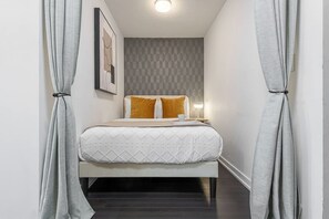 Ein schmales Hotelzimmer mit einem Bett, einem Nachttisch und einer Lampe.
