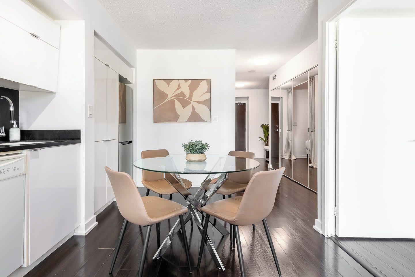 Een moderne keuken met witte kasten, een zwart aanrecht en een glazen eettafel met vier stoelen.