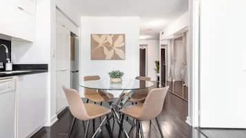 Een moderne keuken met witte kasten, een zwart aanrecht en een glazen eettafel met vier stoelen.