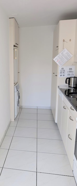 A compact kitchen with a washing machine, a coffee maker, and a cabinet with a paper on the wall. - The Centralstrasse Apartment | Heart of Interlaken (Interlaken)