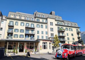 A multi-story hotel with a ground-level restaurant and a red and blue train on the street. - The Centralstrasse Apartment | Heart of Interlaken (Interlaken)