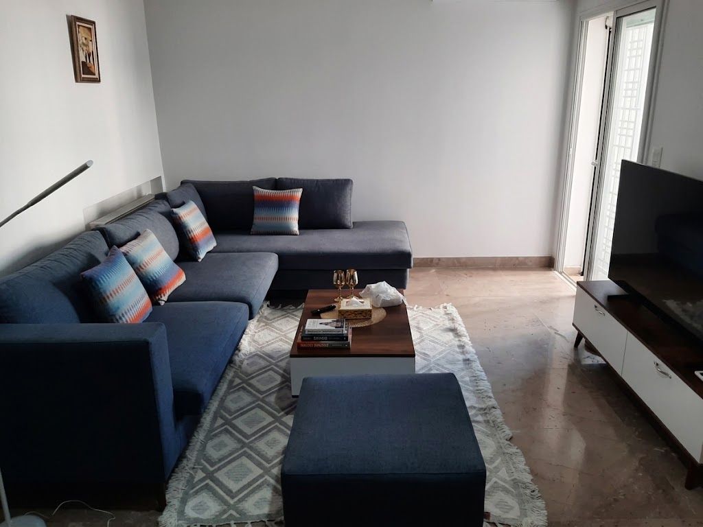 A modern living room with a sectional sofa, a coffee table with books, and a flat-screen TV on a stand.