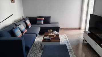 A modern living room with a sectional sofa, a coffee table with books, and a flat-screen TV on a stand.