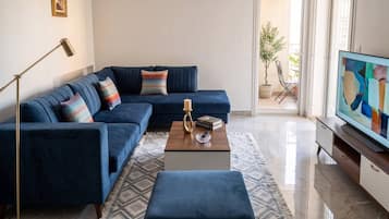 Una sala de estar moderna con un sofá seccional azul, una mesa de centro, una lámpara de pie y un televisor.