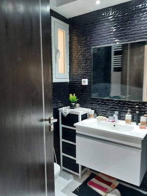 Ein modernes Badezimmer mit schwarzer Fliesenwand, einem weißen Waschbecken und einem Spiegel.
