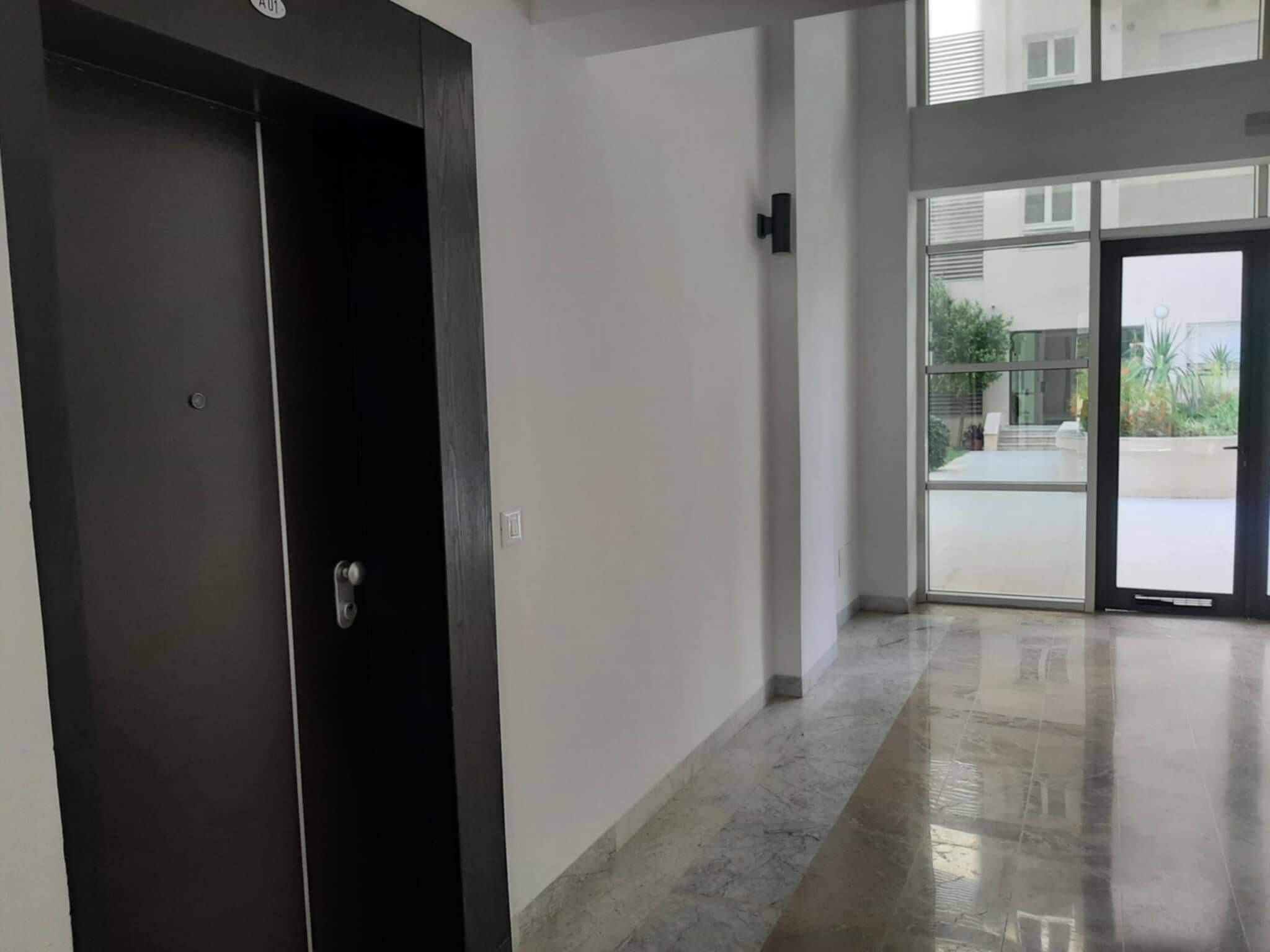 A hallway with a dark door and a glass entrance leading to an outdoor area.