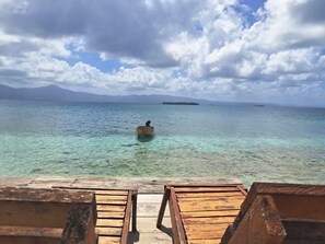 Une terrasse en bois surplombant une mer d’un bleu limpide, avec un bateau visible au loin.