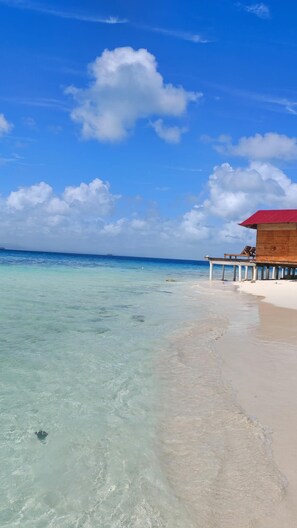 Una playa con agua turquesa cristalina, una estructura de madera con techo rojo y una orilla de arena blanca.