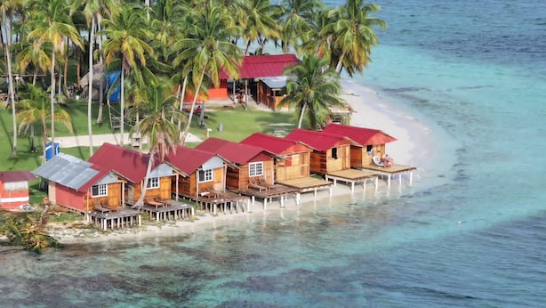 A beachfront property with wooden structures, a pier, and palm trees. - Pelicano Island (Moraquedub)