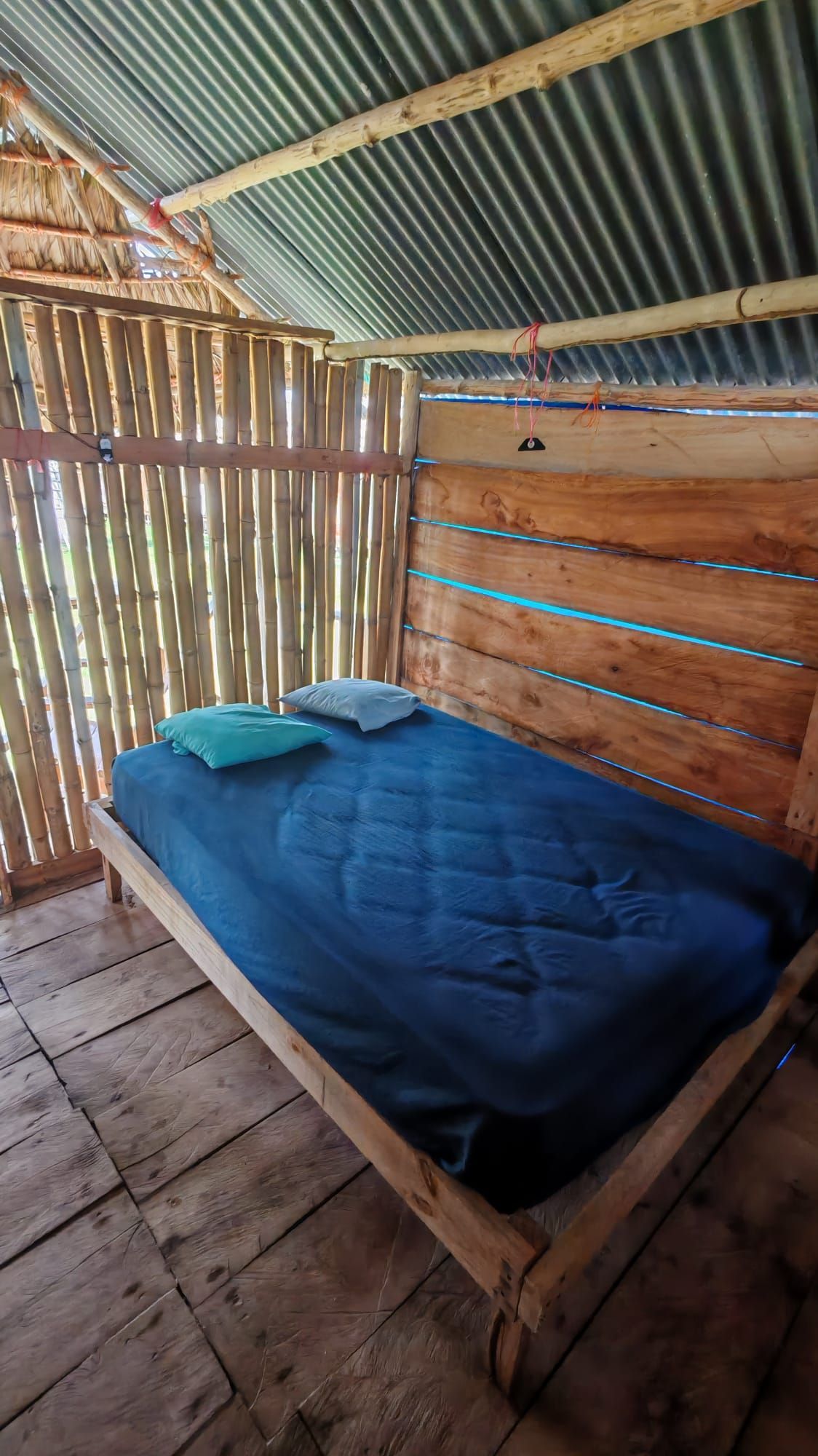 Una cama individual con colchón y almohadas azules, cabecero de madera y valla de bambú.